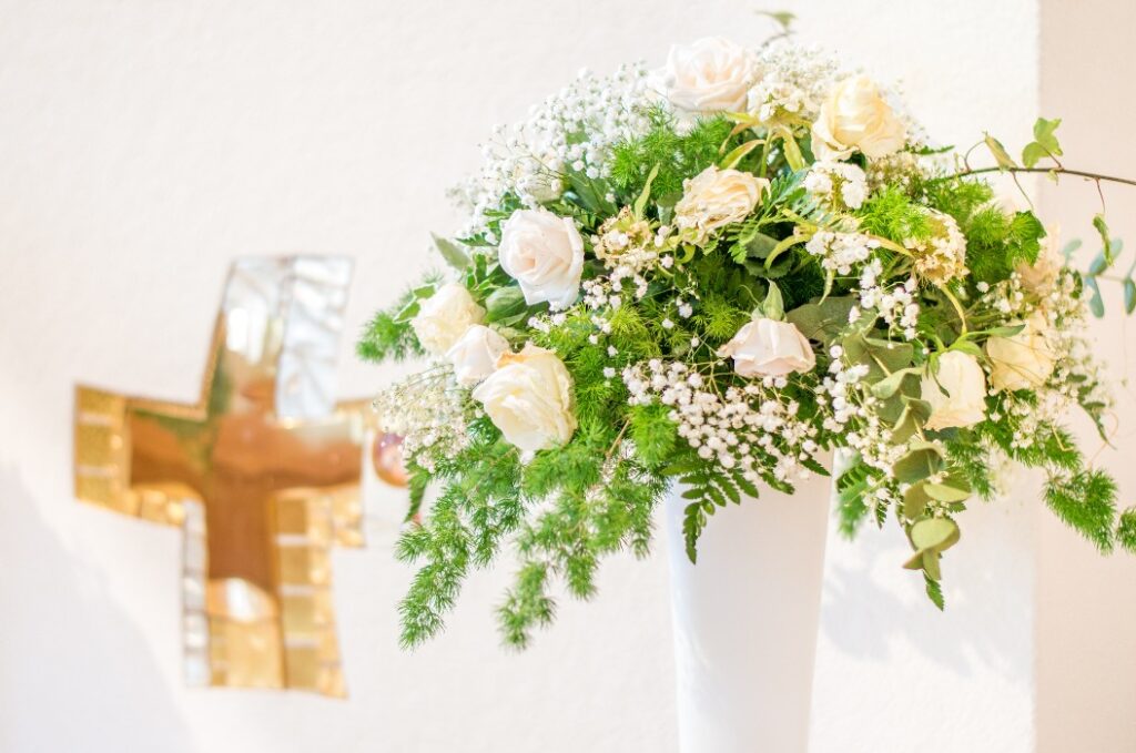 A wedding bouquet of white flowers in front of the white altar with a golden cross. Symbol of purity and innocence.