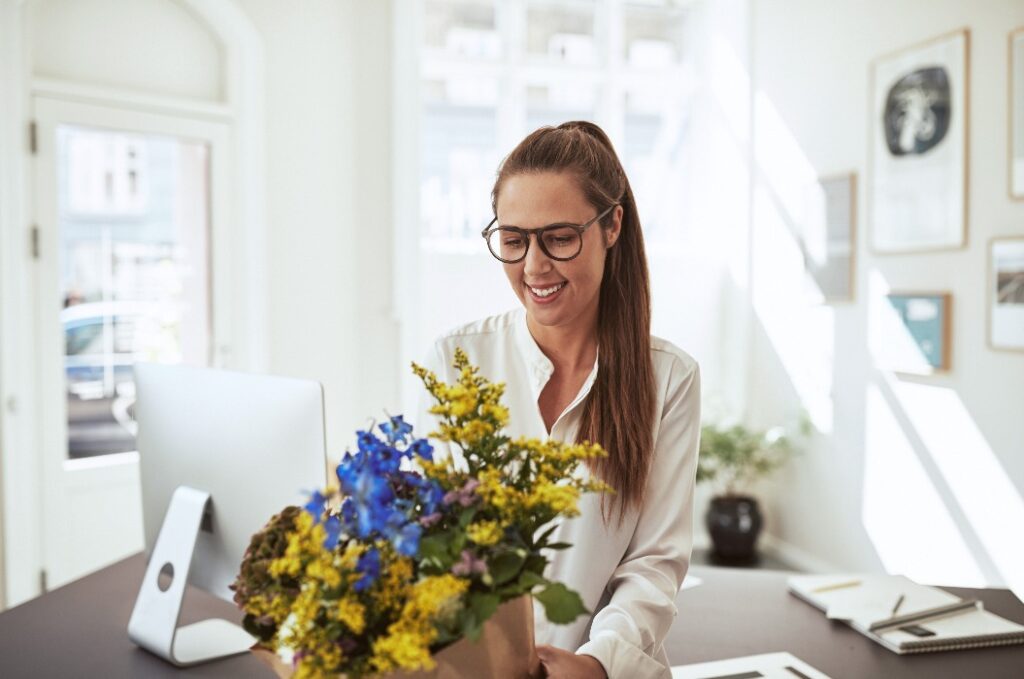 Smiling young female architect standing with flowers in her offi