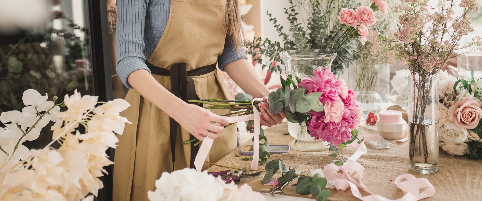 woman florist in beige apron is working in  flower shop. Floral design studio, making decorations and arrangements. Flower delivery, order creation. Small business.